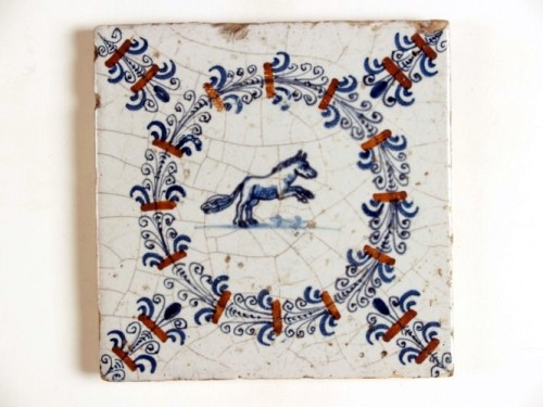 Tegel met blauwwit decor van een paard in een polychrome aigrettenkrans